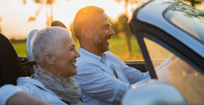 Retired couple driving in a convertible car.